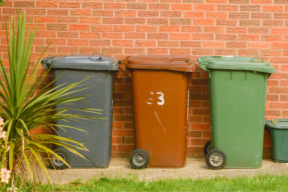 Image of three wheelie bins stored by a red brick wall